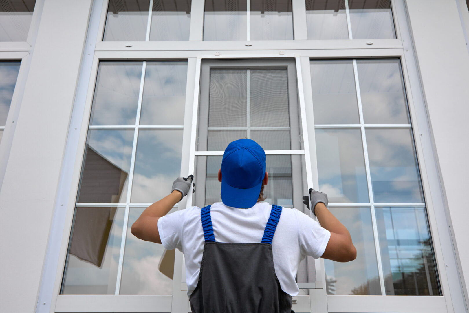 Man installing a window screen outside house.