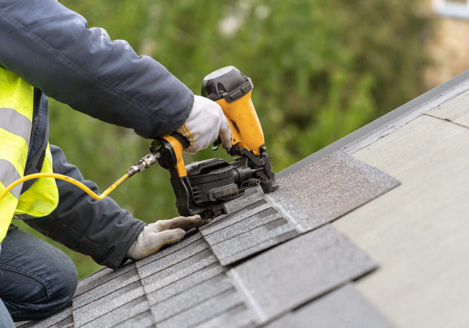 Workman using pneumatic nail gun install tile on roof of new house under construction Worker using nail gun on roof shingles.