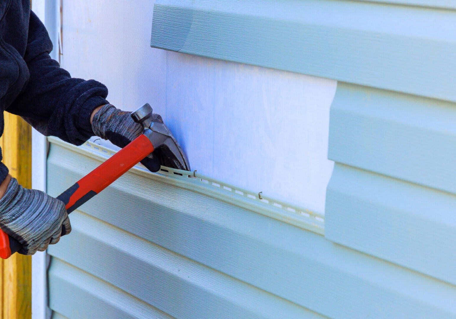 An exterior wall of a house was covered in plastic siding that needed to be replaced Person installing vinyl siding with hammer.